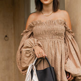 Woman wearing a beige smocked dress holding a black handbag.