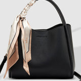 Black handbag with a decorative ribbon on a light gray background