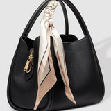 Black handbag with a beige scarf draped over it on a light gray background