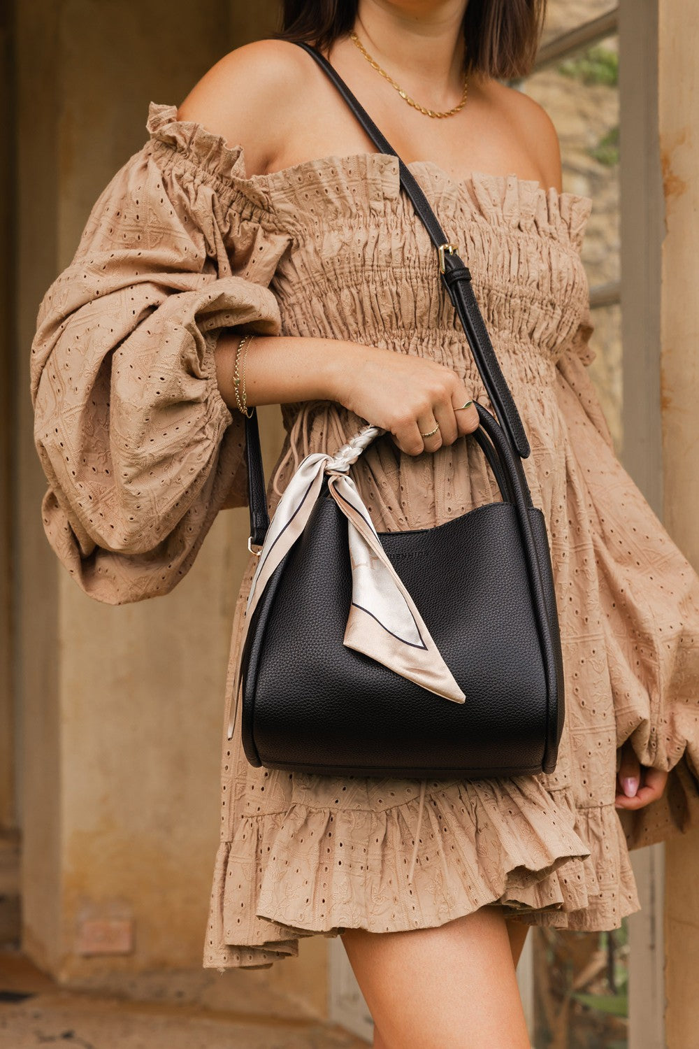 Woman holding a black handbag wearing a beige off-shoulder dress.