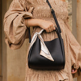 Woman holding a black handbag wearing a beige off-shoulder dress.