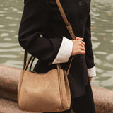 Person wearing a black coat and holding a tan handbag by a body of water.