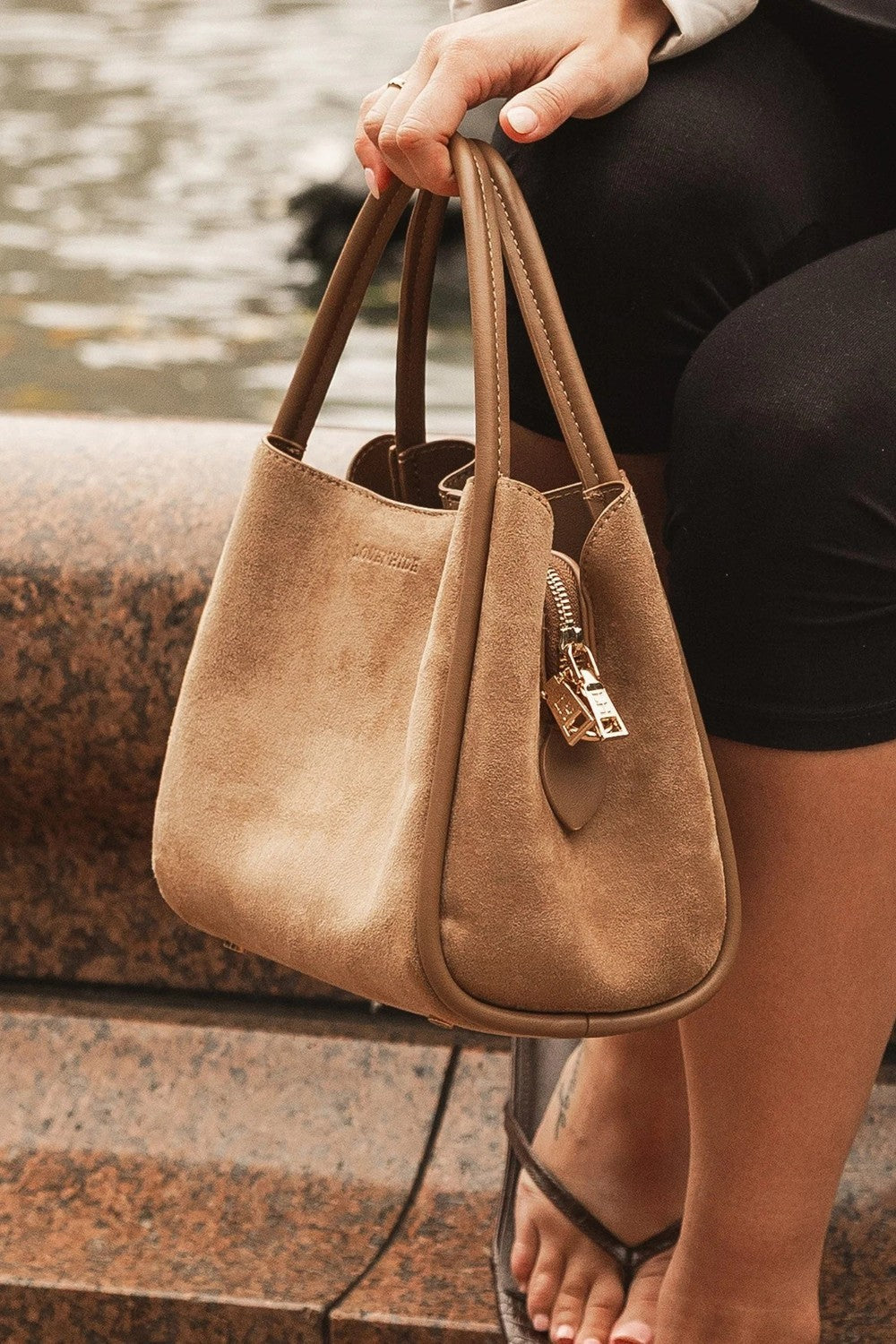 Brown handbag held by a person sitting on steps near water