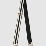 Black and white striped bag strap with gold hardware on a light gray background