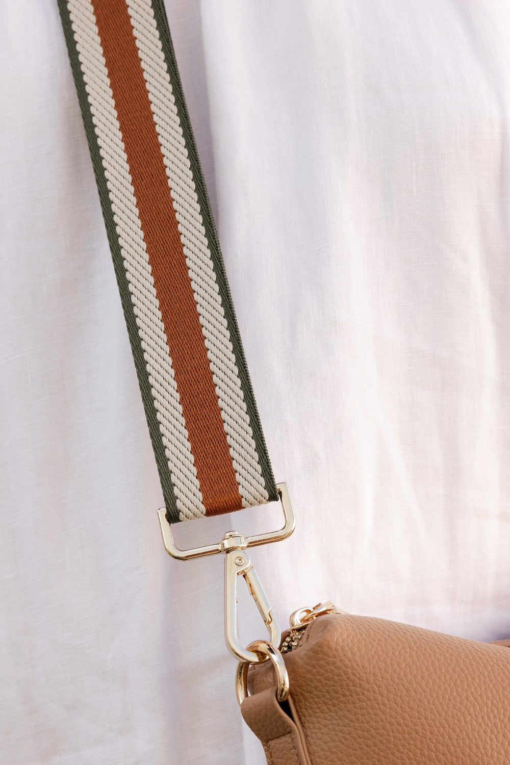 Close-up of a brown handbag with a strap featuring green, brown, and beige colors on a light background.