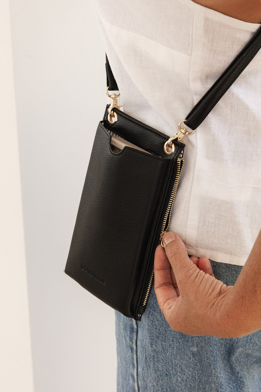 Person holding a black crossbody bag with gold zippers against a light background