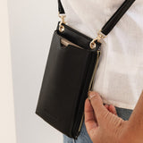 Person holding a black crossbody bag with gold zippers against a light background
