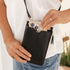 Person holding a black crossbody bag with a phone case on a blurred background