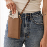 Person holding a phone in a brown phone case with a beige background