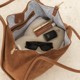 Brown handbag with sunglasses, phone, and lip products on a light background