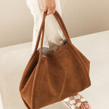 Brown suede handbag held by a person on a light background