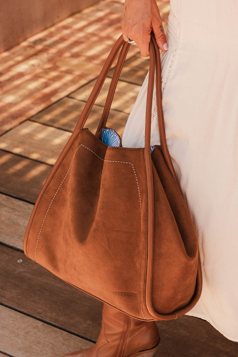 Brown pleather tote bag held by a person on a wooden floor