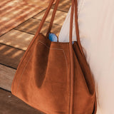 Brown pleather tote bag held by a person on a wooden floor
