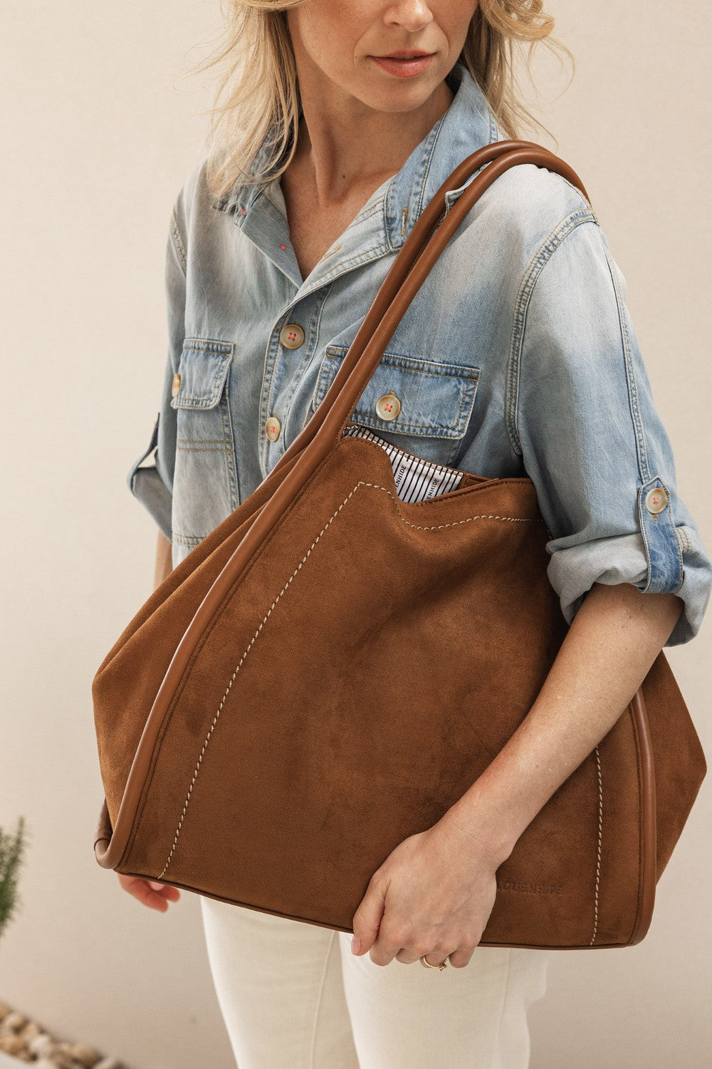 Woman holding a brown pleather tote bag against a neutral background