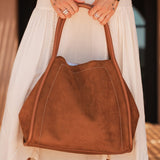 Brown pleather handbag held by a person wearing a white dress and brown boots.