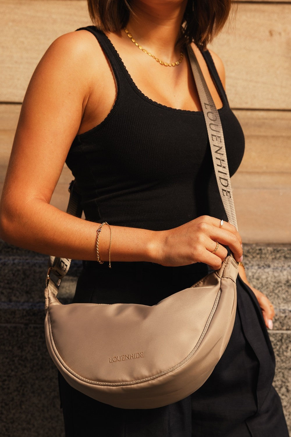 Person holding a beige shoulder bag with 'LOUENHIDE' branding.