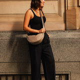 Woman in black outfit with beige bag standing against a building.