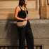 Woman in black outfit with beige bag standing against a building.