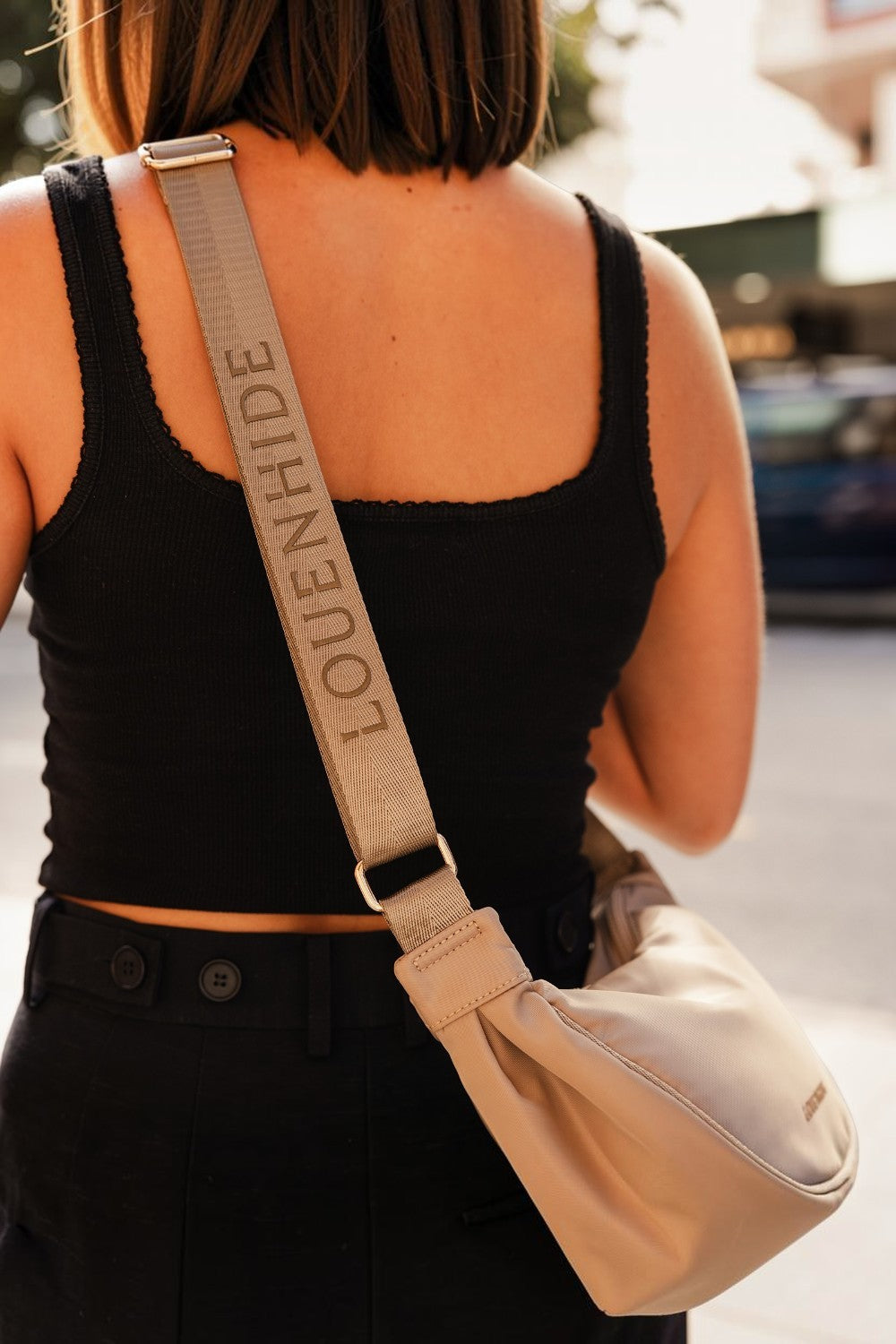 Person wearing a black tank top and carrying a beige crossbody bag with 'LOUENHIDE' branding.