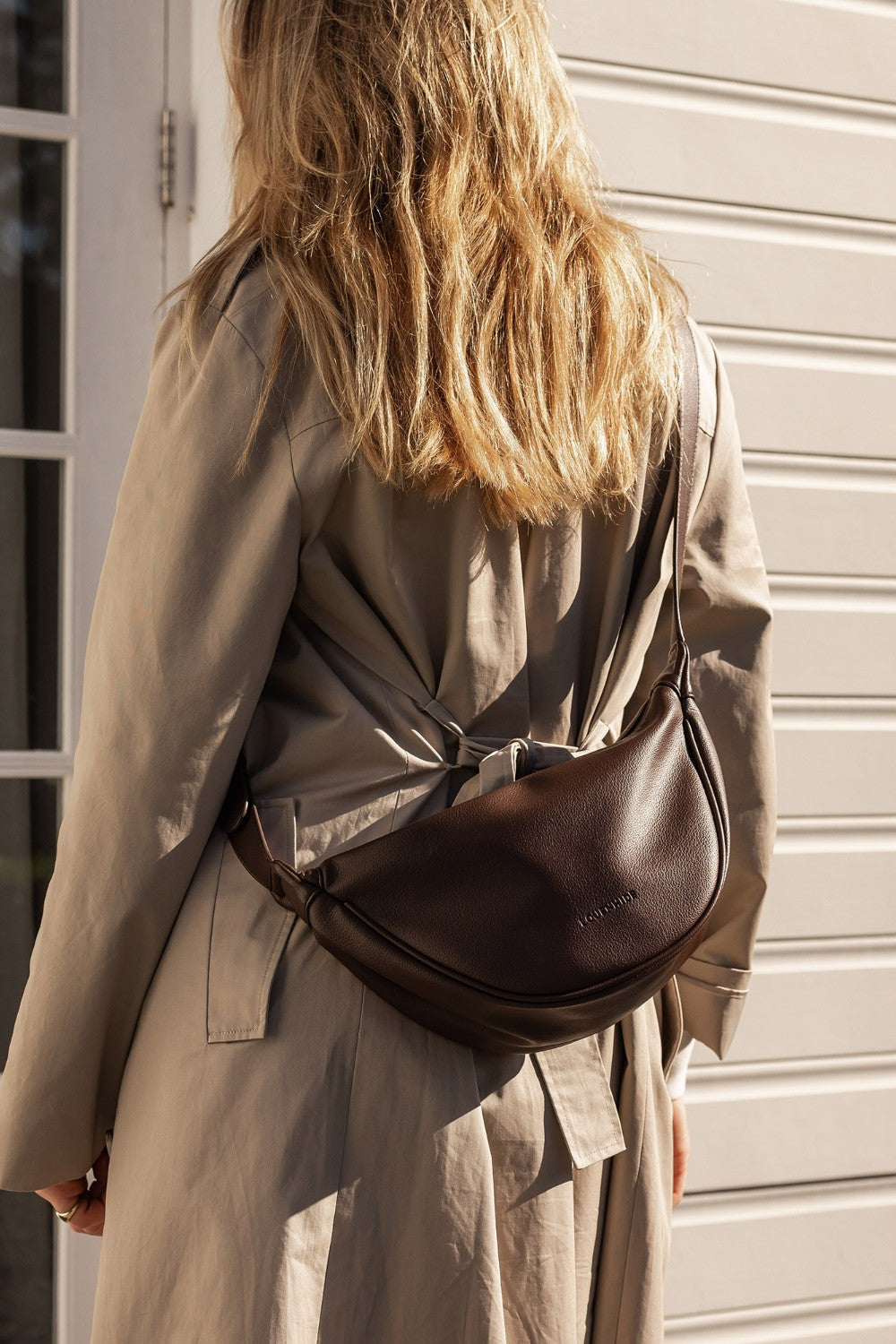 Person wearing a beige trench coat with a brown pleather bag over their shoulder.