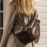 Person wearing a beige trench coat with a brown pleather bag over their shoulder.