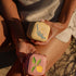 Two small, embroidered pouches held by a person against a natural background.