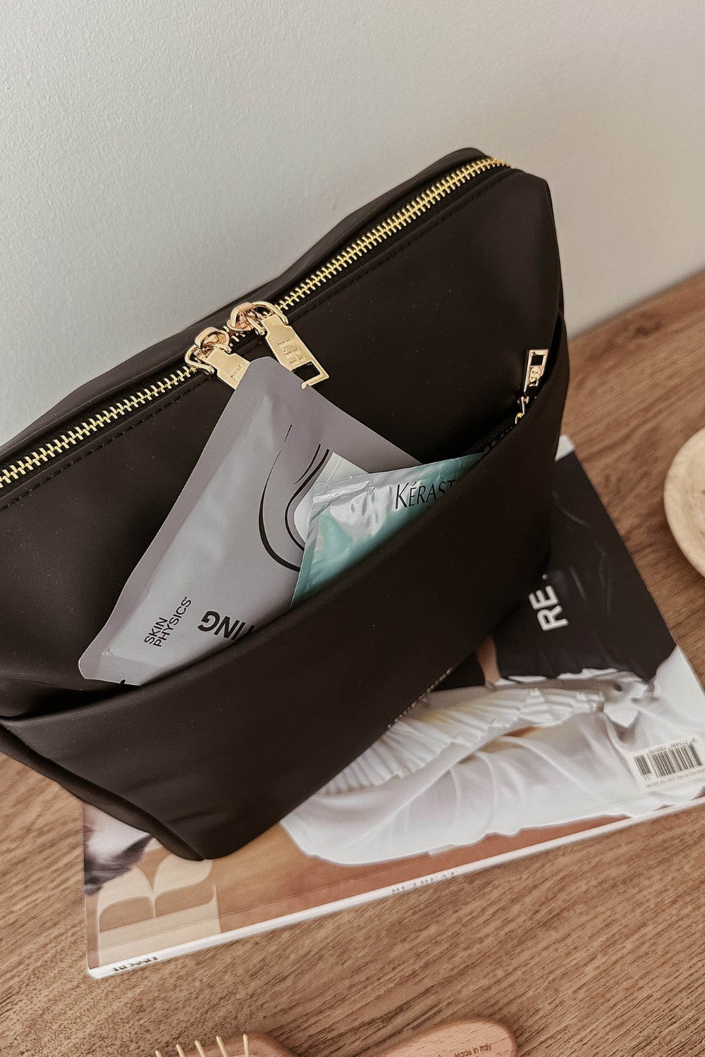 Black pouch with gold zipper on a wooden surface with magazines underneath