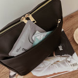 Black pouch with gold zipper on a wooden surface with magazines underneath