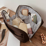 Open brown pleather bag with striped lining containing travel-sized products on a wooden surface.
