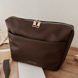 Brown pleather bag on a wooden surface with a magazine underneath