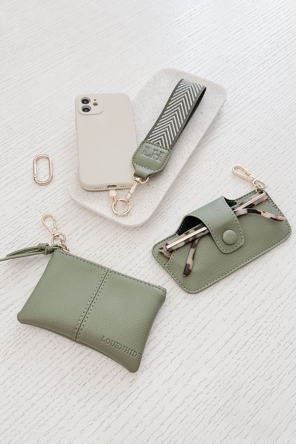 Set of green pleather accessories including a pouch, keychain, and phone case on a white textured background.