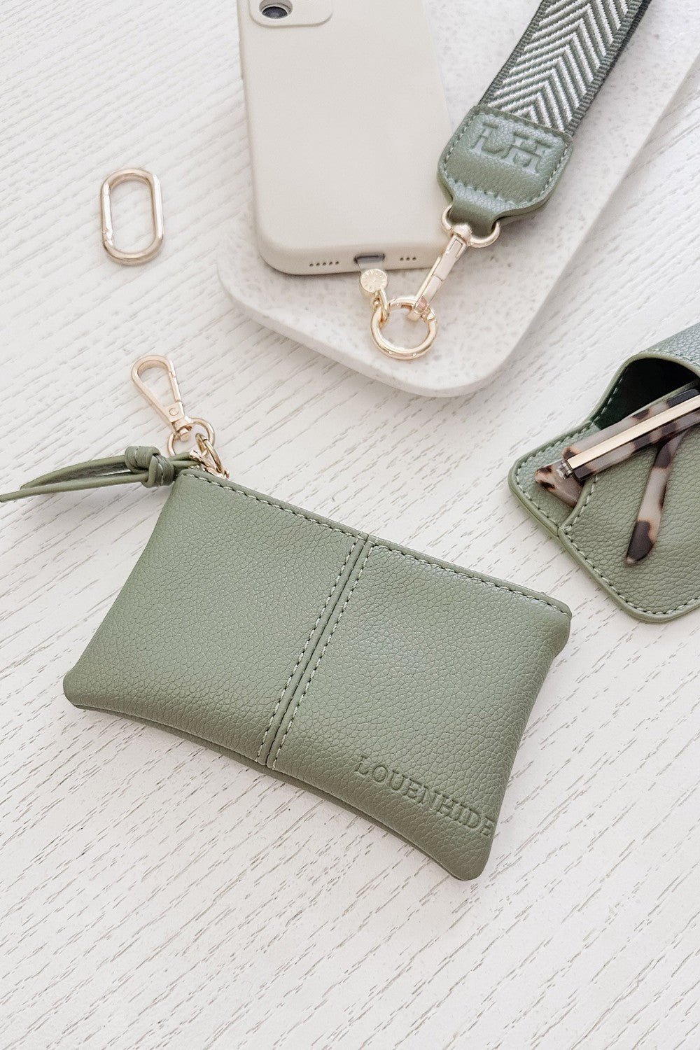 Green pleather pouch with keychain and phone holder on a textured white surface