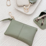Green pleather pouch with keychain and phone holder on a textured white surface