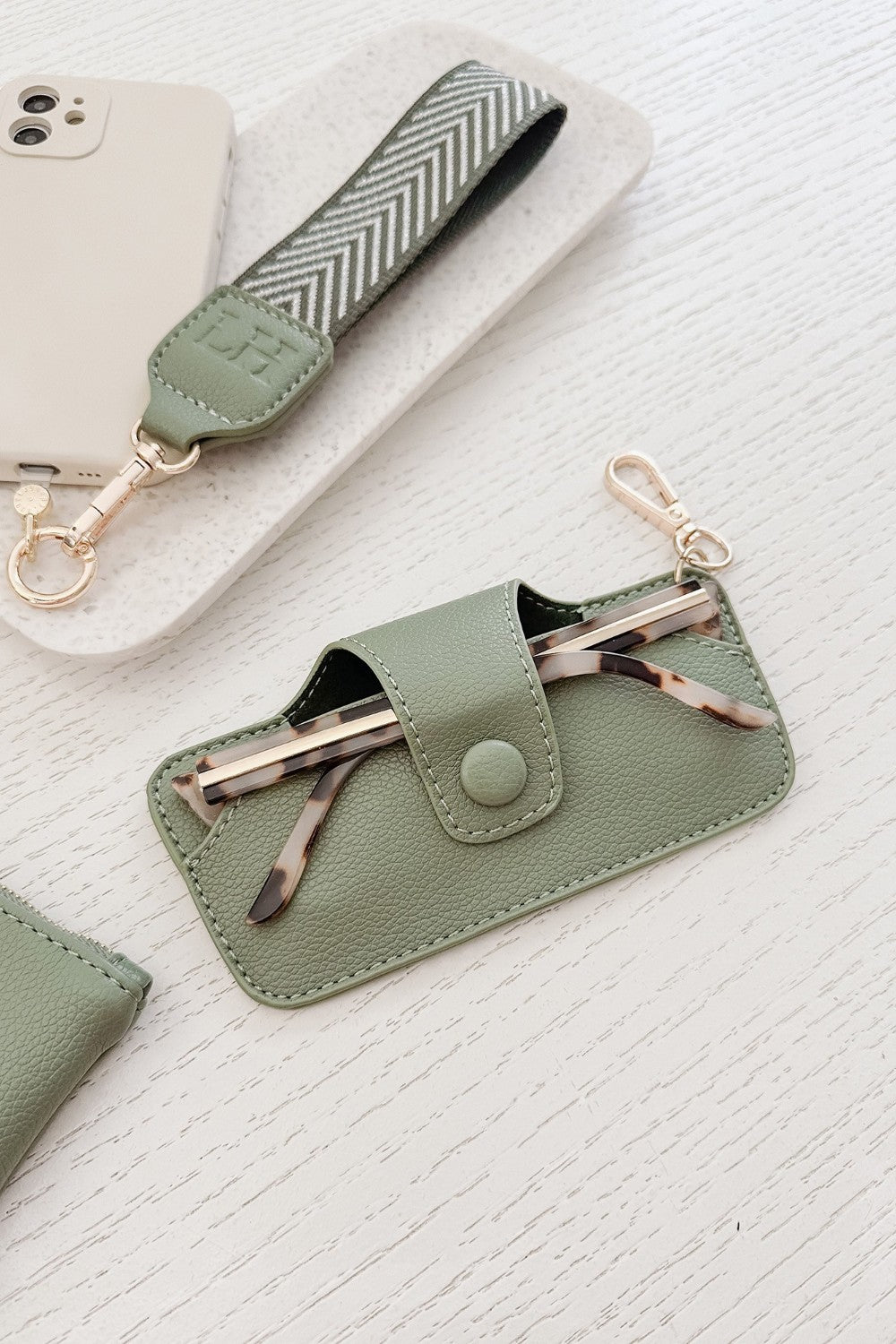 Green phone case with keychain and glasses holder on a textured white surface