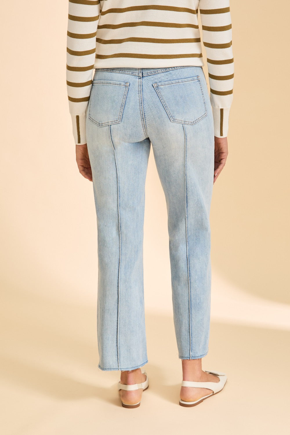 Person wearing striped sweater with blue jeans on beige background