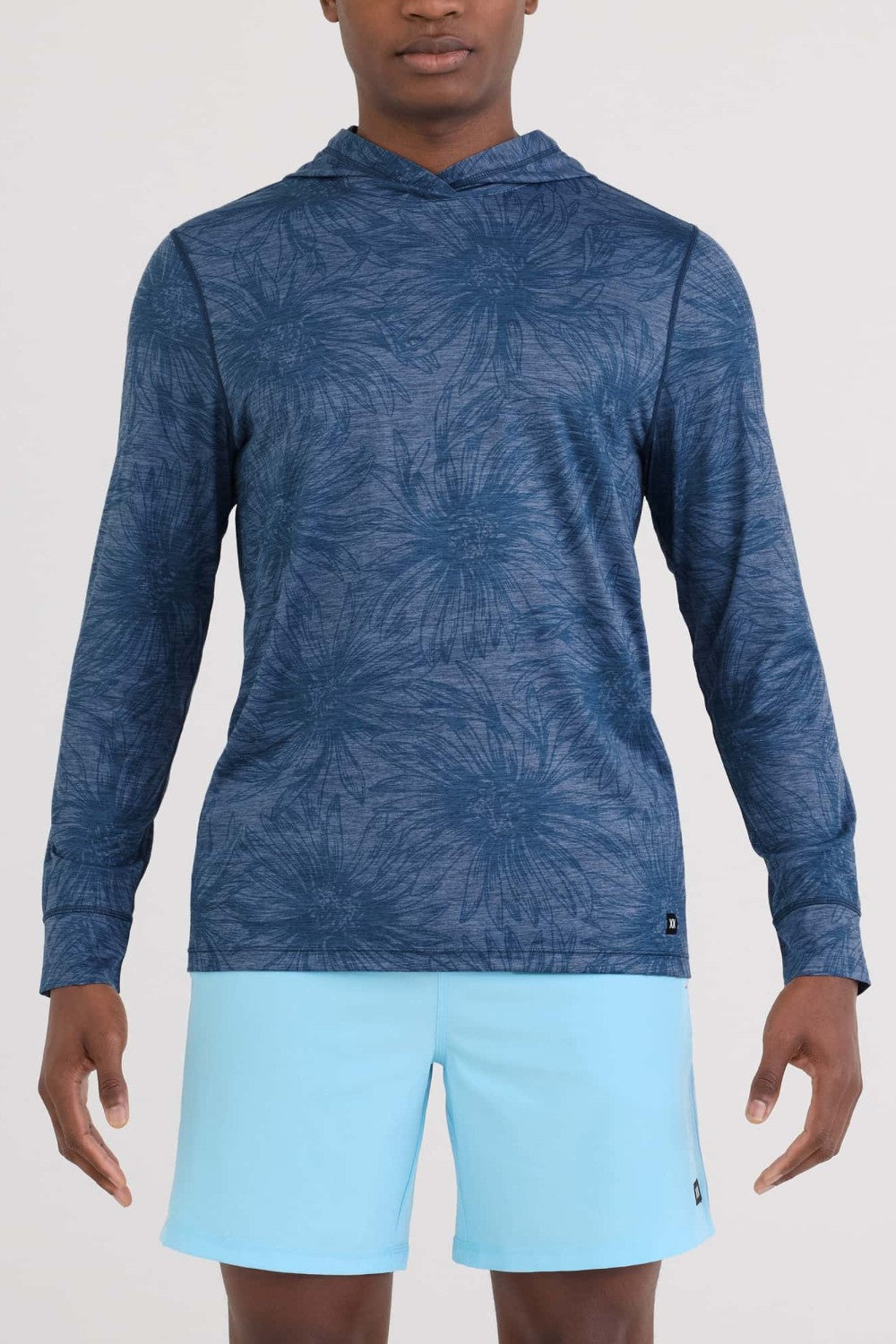 Person wearing a blue patterned long-sleeve shirt and light blue shorts on a white background