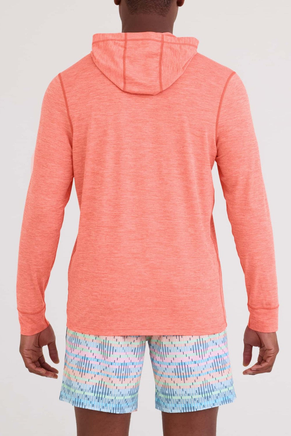 Person wearing a coral hoodie and patterned shorts on a white background