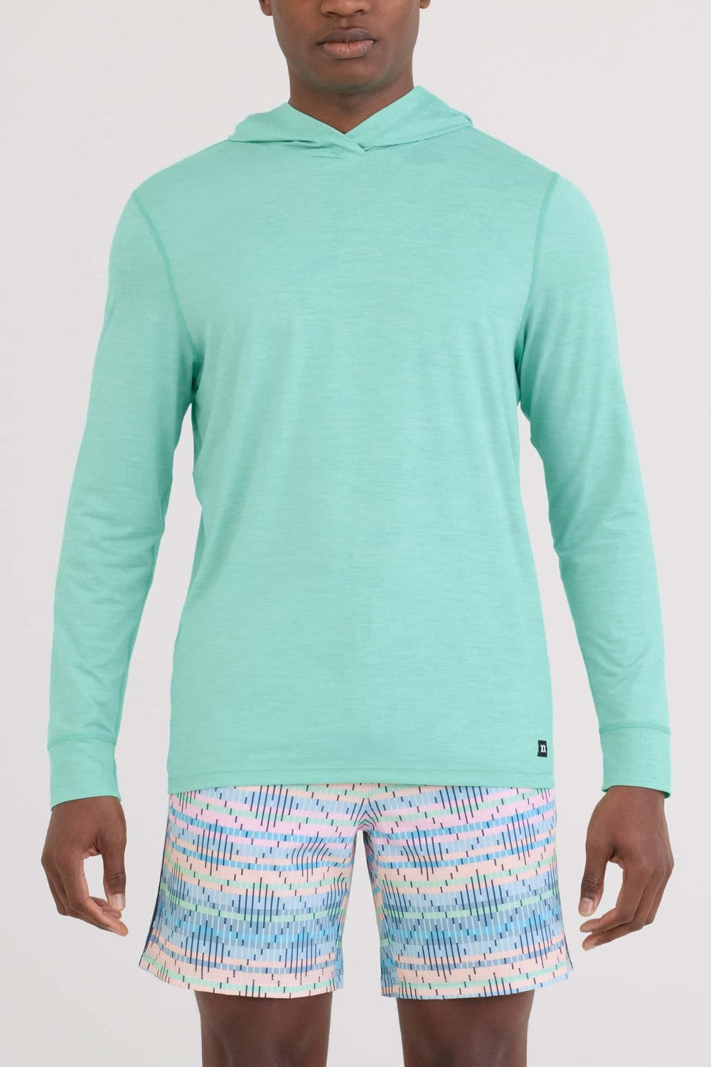 Person wearing a teal long-sleeve shirt and patterned shorts on a white background
