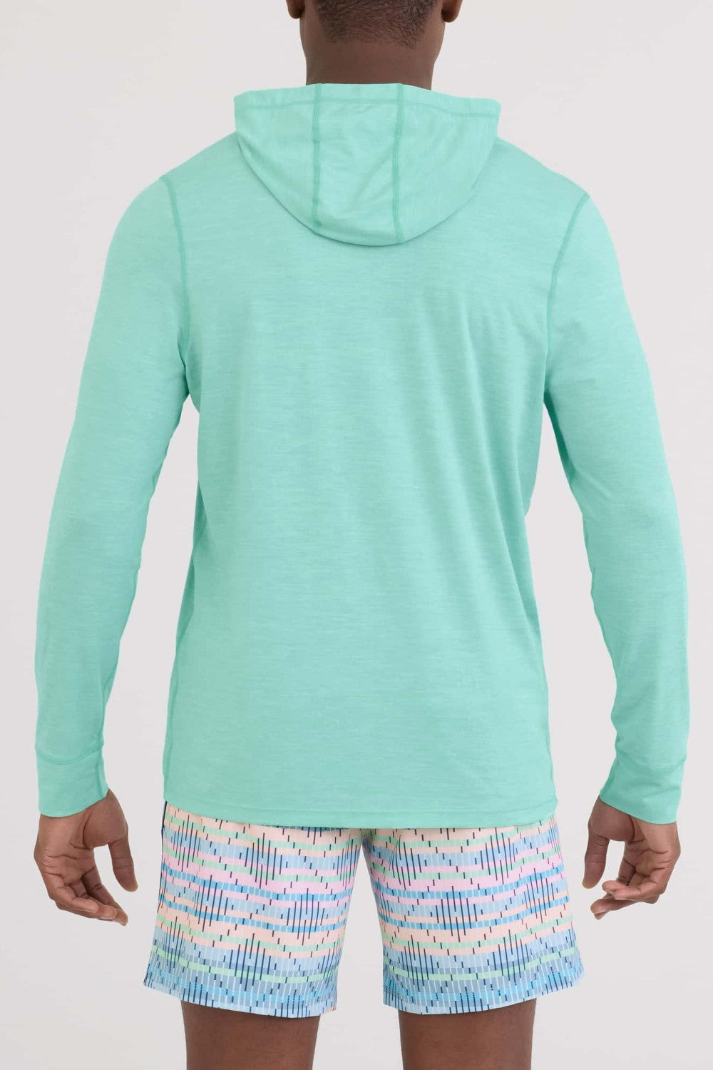 Person wearing a light blue hoodie and patterned shorts on a plain background