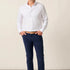 Man wearing a white dress shirt and navy pants against a beige background