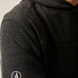 Close-up of a person wearing a dark gray long-sleeve shirt with a logo on the sleeve.