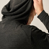 Person wearing a dark gray hoodie adjusting the hood against a neutral background