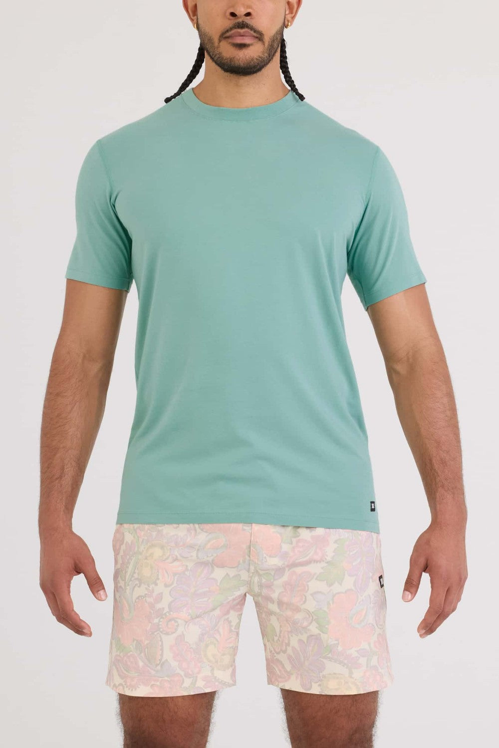 Man wearing a teal t-shirt and patterned shorts on a white background