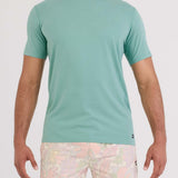 Man wearing a teal t-shirt and patterned shorts on a white background