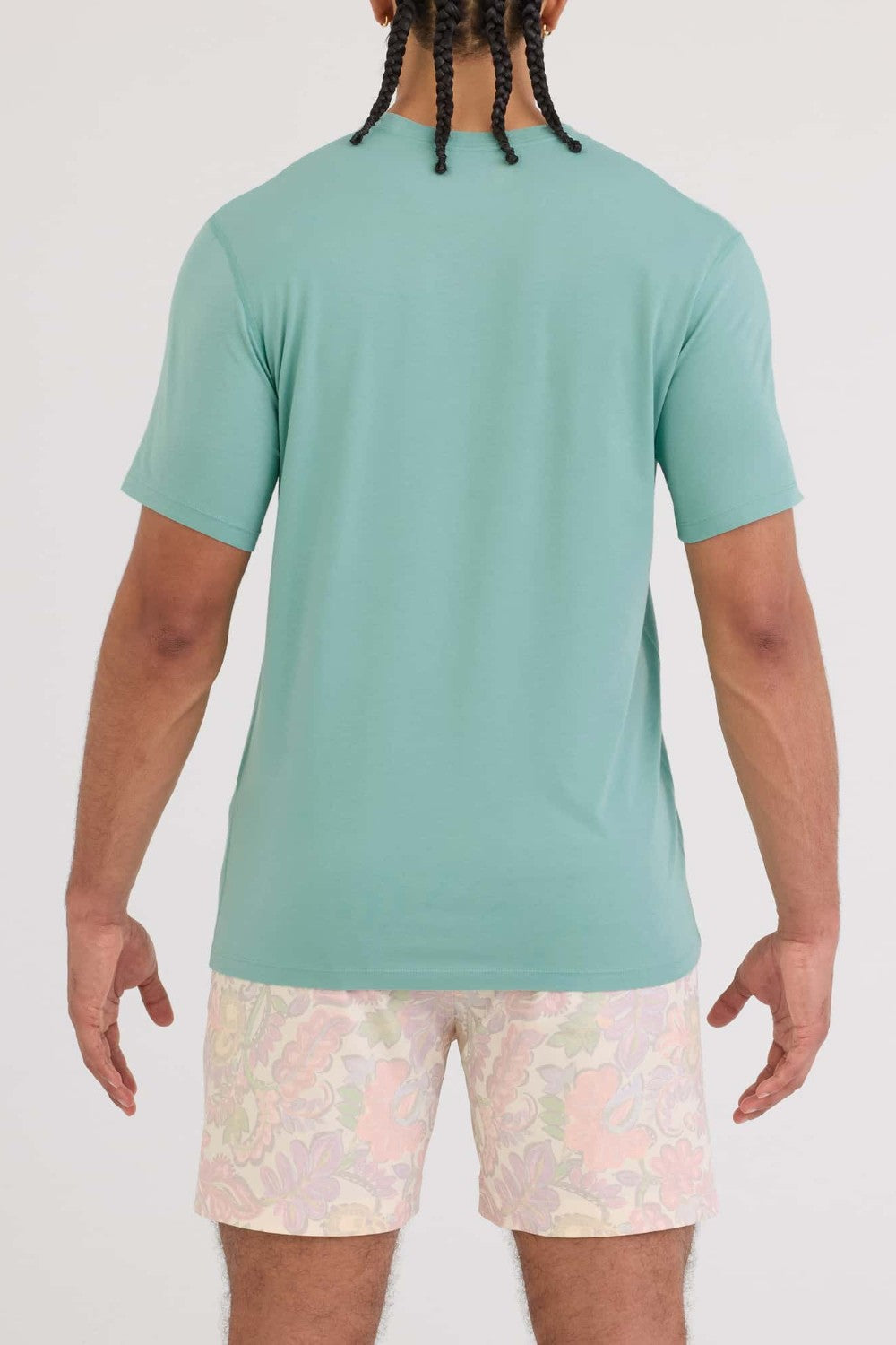 Person wearing a light green t-shirt and patterned shorts on a white background