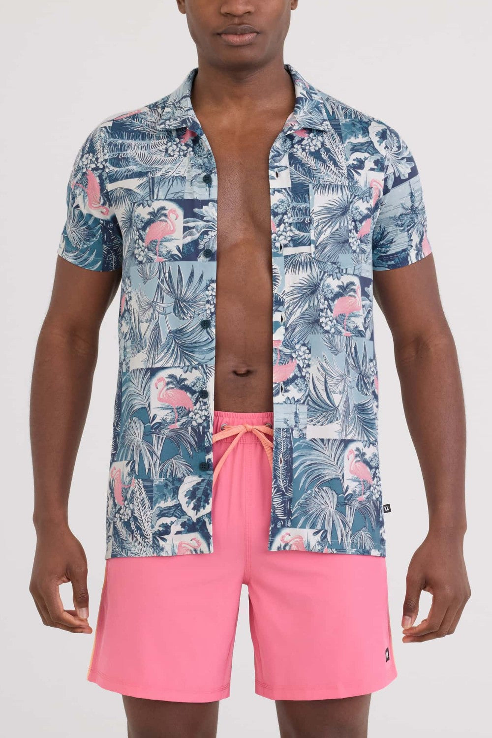Man wearing a blue floral shirt with open collar and pink shorts on a white background