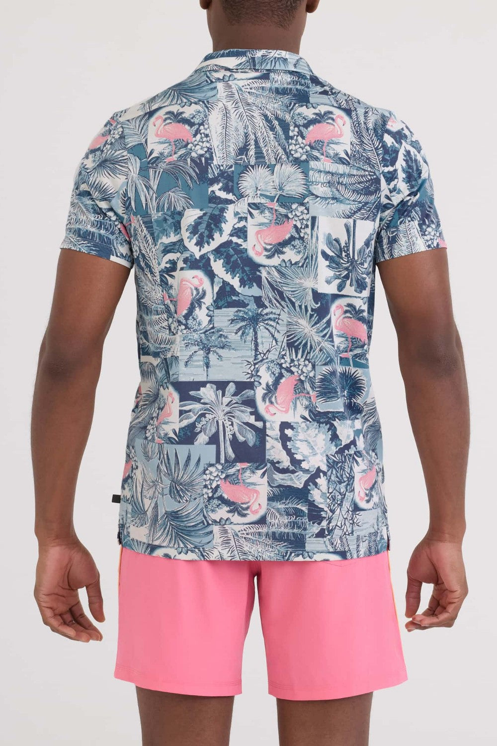 Person wearing a tropical patterned shirt and pink shorts on a white background