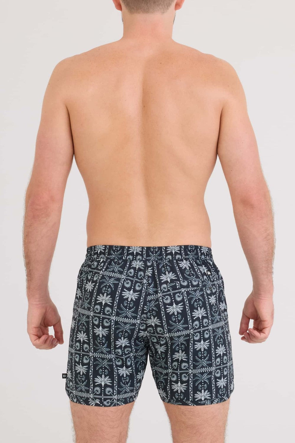 Man wearing navy blue swim shorts with white pattern on a plain background