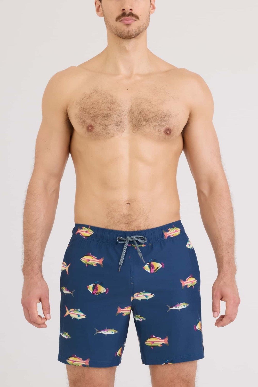 Man wearing navy blue swim shorts with colorful fish pattern on a white background