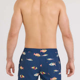 Man wearing navy blue swim shorts with colorful fish pattern on a white background